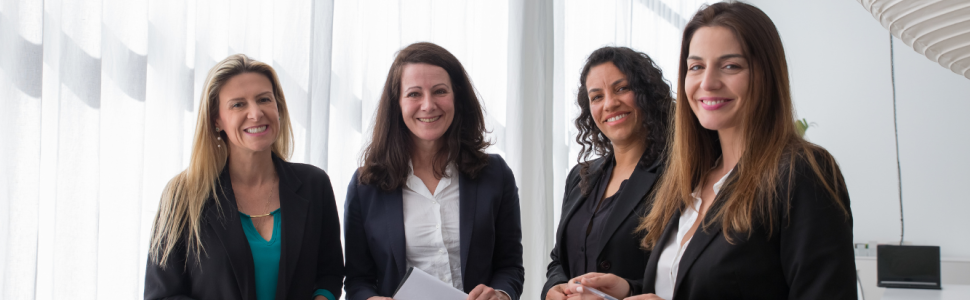 Four senior executive women stand together smiling