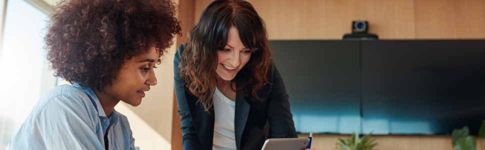 Two professional women look at a device screen.