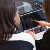 Two women at a computer, one pointing at code