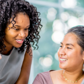 Three diverse women smiling and having a conversation at a conference table.