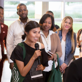 Woman is speaking to a large group in a professional work environment.