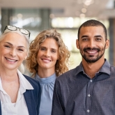 Seven business people - men and women - standing in a line facing the camera and smiling.