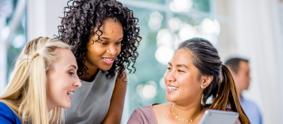 Three diverse women smiling and having a conversation at a conference table.