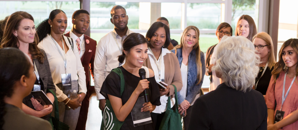 Woman is speaking to a large group in a professional work environment.