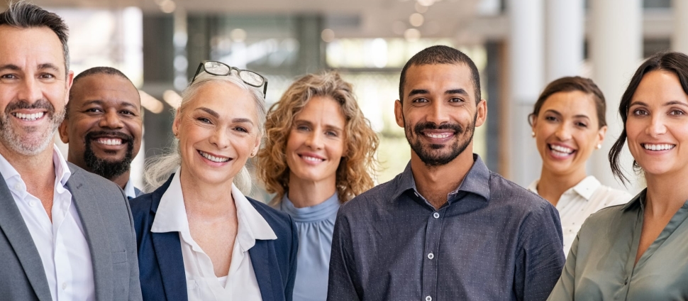 Seven business people - men and women - standing in a line facing the camera and smiling.