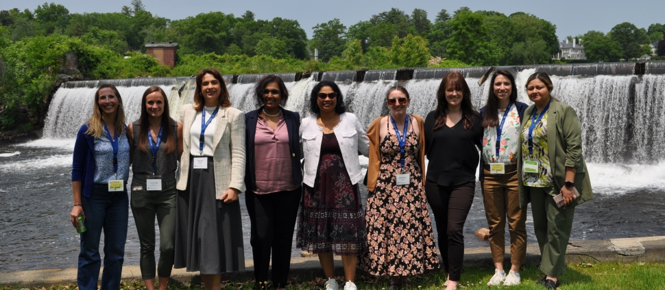 A diverse group of business women smiling at the camera in front of the Smith College waterfall.