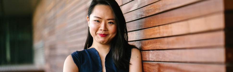 Professional woman leaning against a wood paneled wall and smiling.