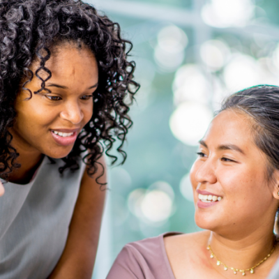 Three diverse women smiling and having a conversation at a conference table.