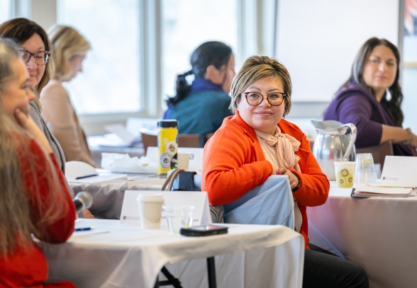 A woman in an orange jacket is listening to a speaker during a professional development seminar